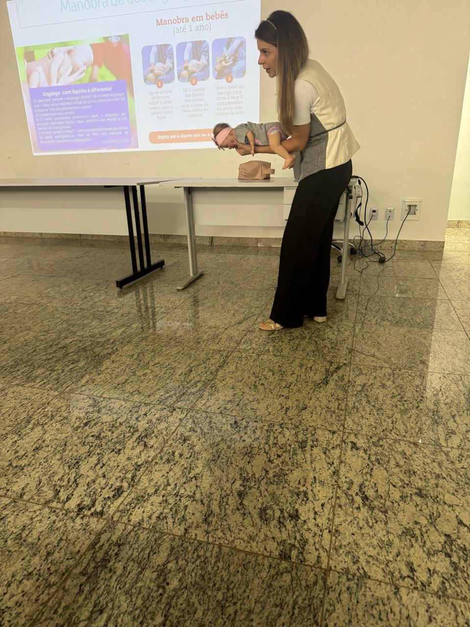 Dra. Halana ministrando o curso de Suporte Básico de Vida, demonstrando a manobra de desengasgo em um boneco de bebê